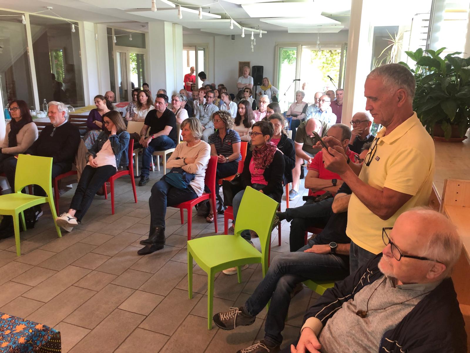 Felice in basso a destra seduto insieme a una quarantina di persone che ascoltano un relatore che non si vede